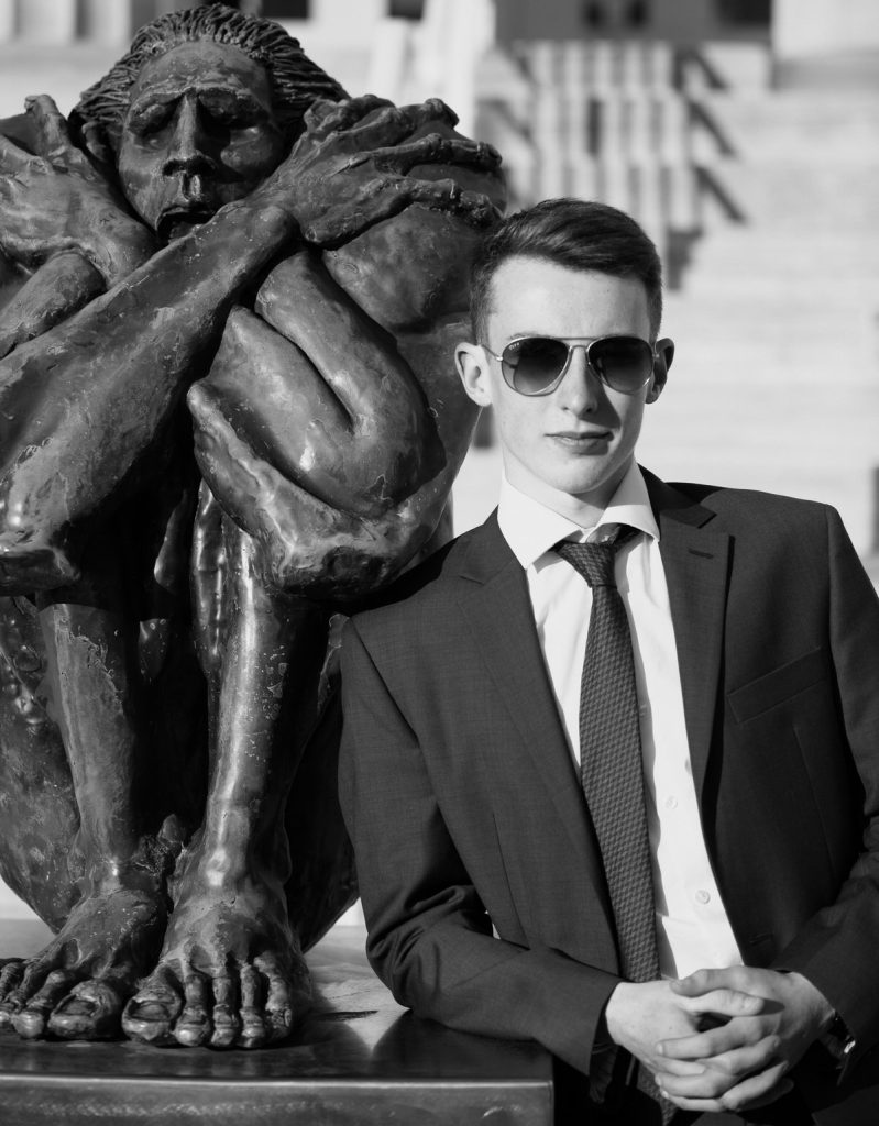 Boy in suit and sunglasses leans against statue for senior portraits in Erie, PA