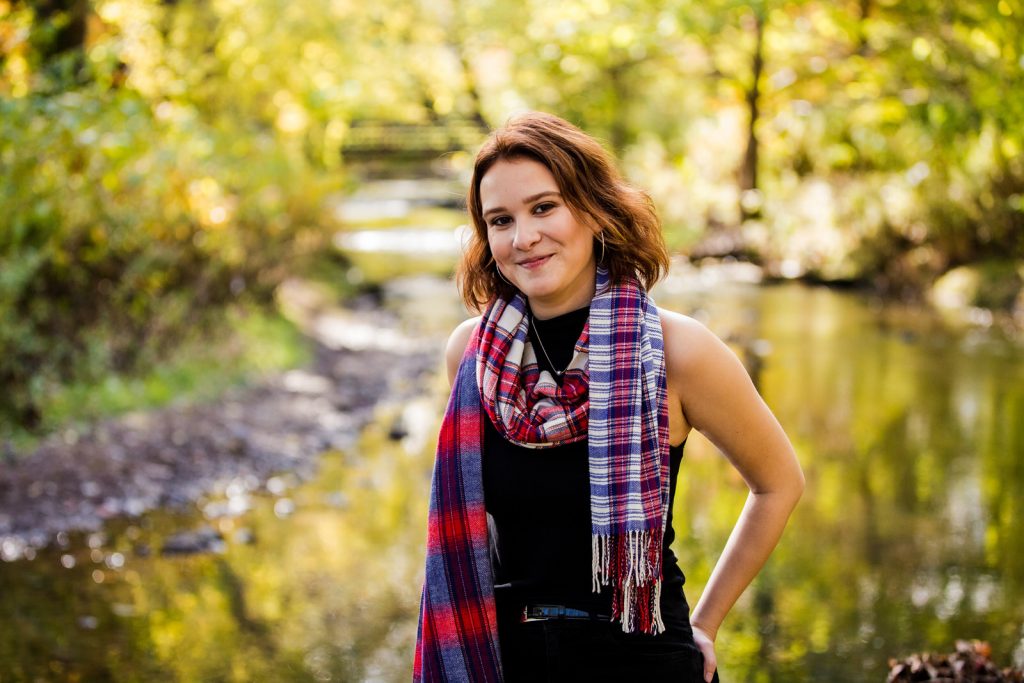 Girls wearing a plaid scarf stands next to a creek in Frontier Park senior portraits in Erie PA