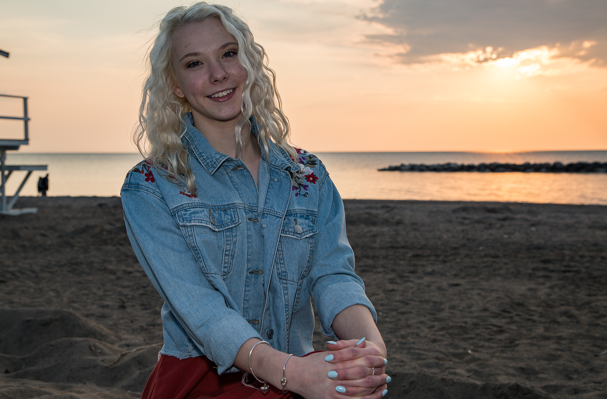 Girl wearing jean jacket sitting on the beach for Sweet Sixteen photos at Presque Isle State Park