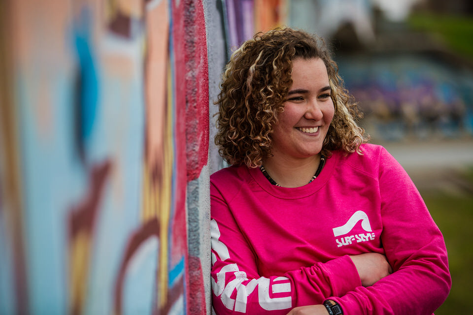 Girl in bright pink shirt smiles while standing against a graffiti wall