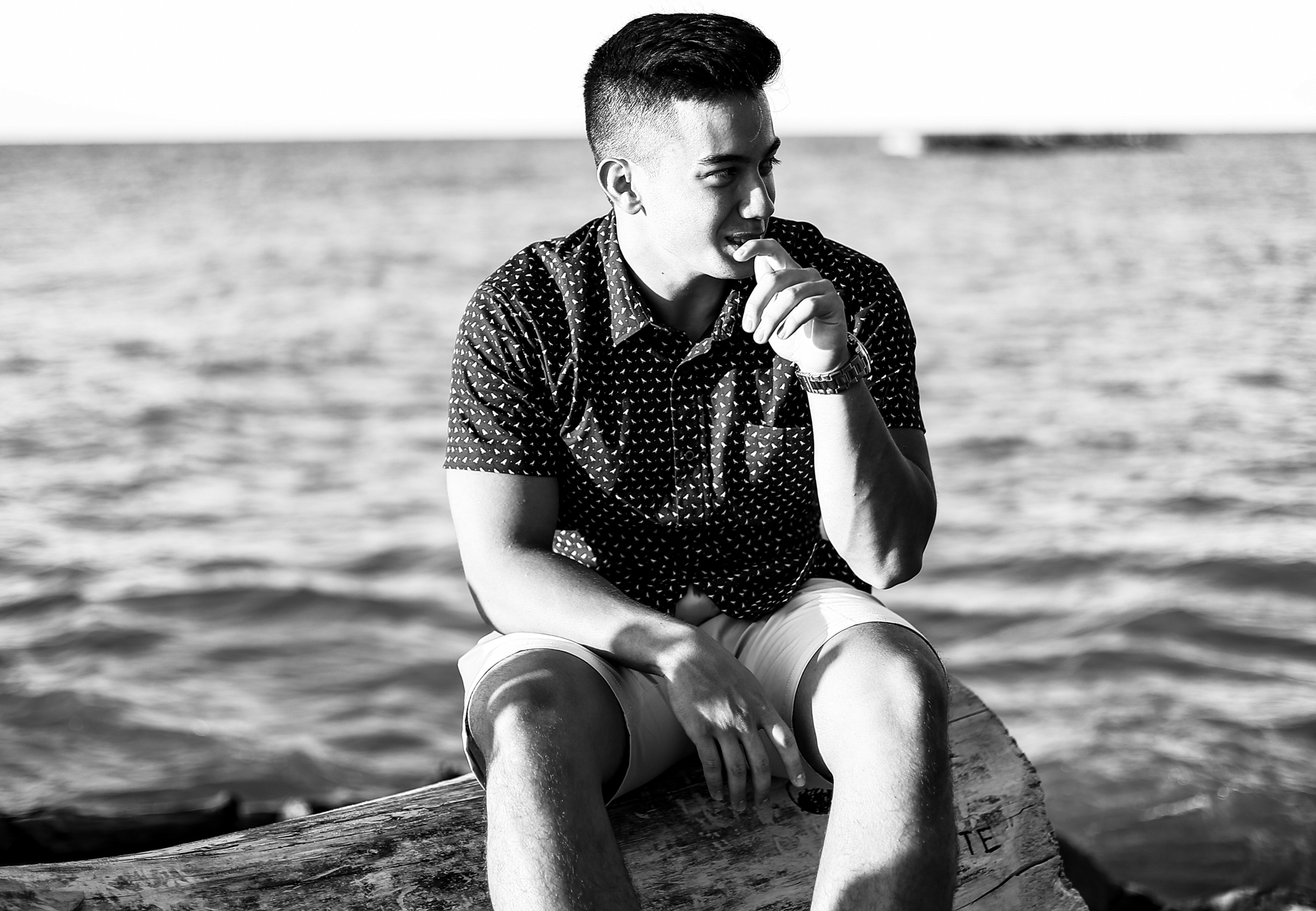 Young man sits on driftwood during Presque Isle senior portraits