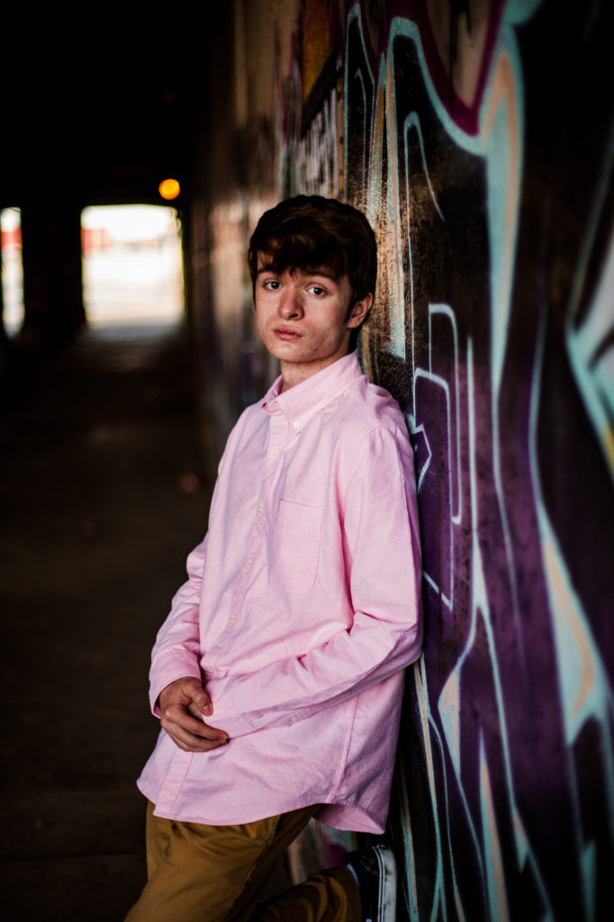 Boy leaning against graffiti filled wall for senior photos in Downtown Erie