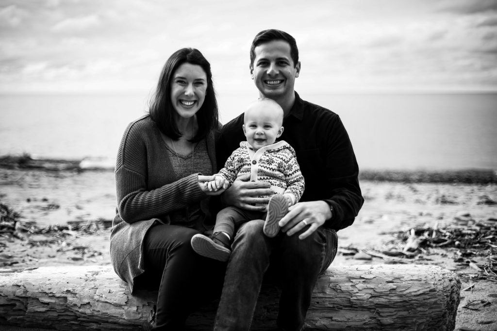 Mother, father and baby sit on driftwood for family photos at Presque Isle
