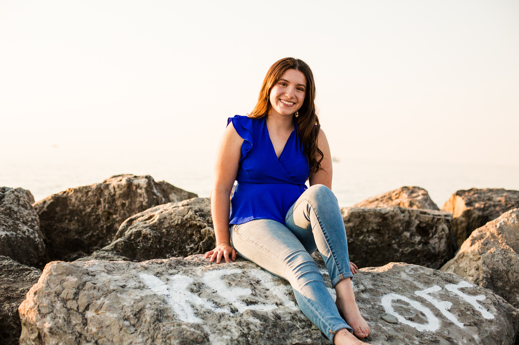 Smiling girl sits on rock at Presque Isle beach for summer portraits