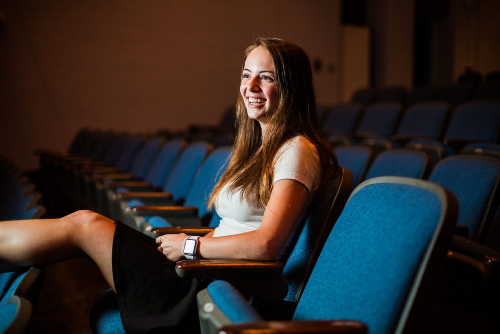 Laughing girl sits in theatre seats for senior portraits