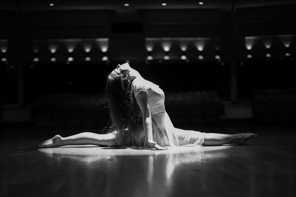 A stage's spotlight highlights a dancer in a full split with head tilted back