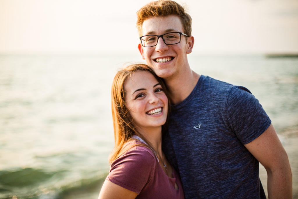 High school boy and girl pose together next to Lake Erie on a Presque Isle beach at sunset 