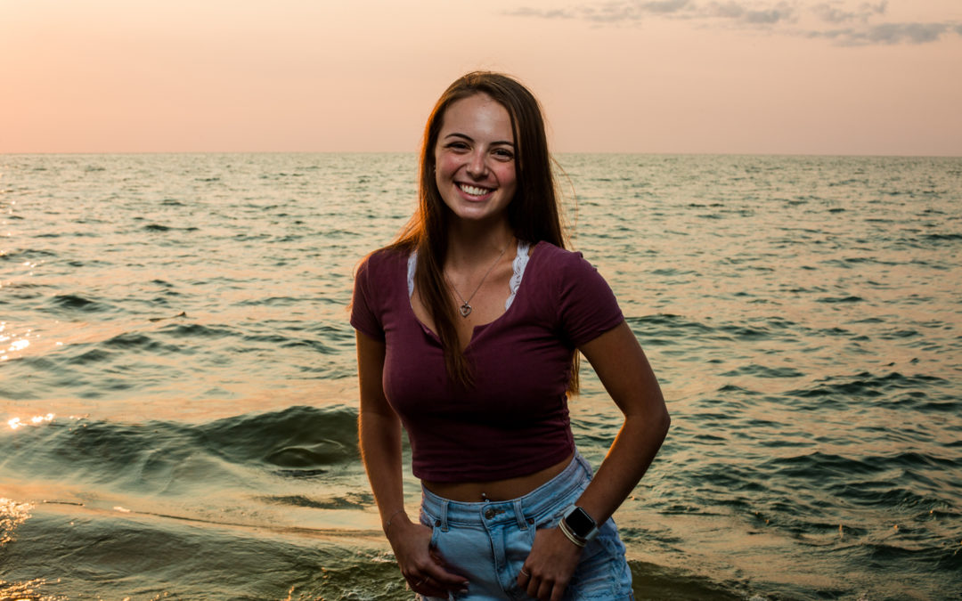Girl stands next to lake at sunset for senior photos on a Presque Isle Beach