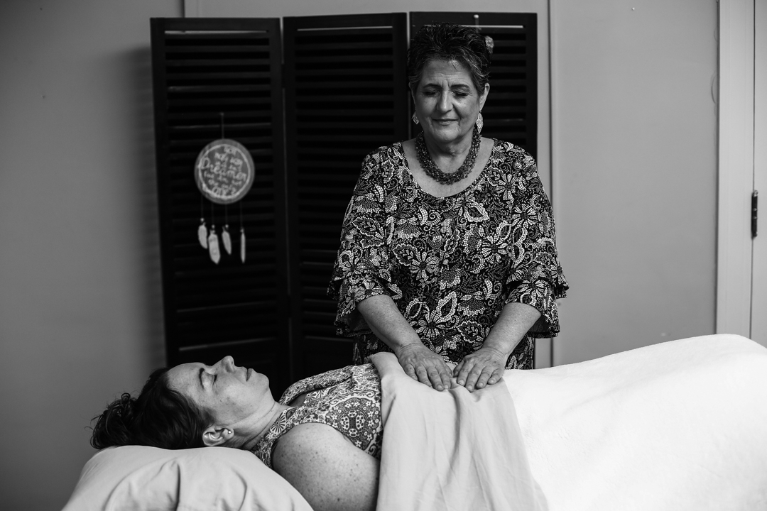 A woman standing with her hands on a woman lying on a treatment table covered in a blanket. Taken by a professional photographer.