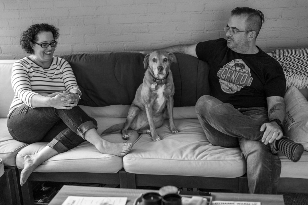 A woman, a dog, and a man on a couch in black and white. Taken by a professional photographer.